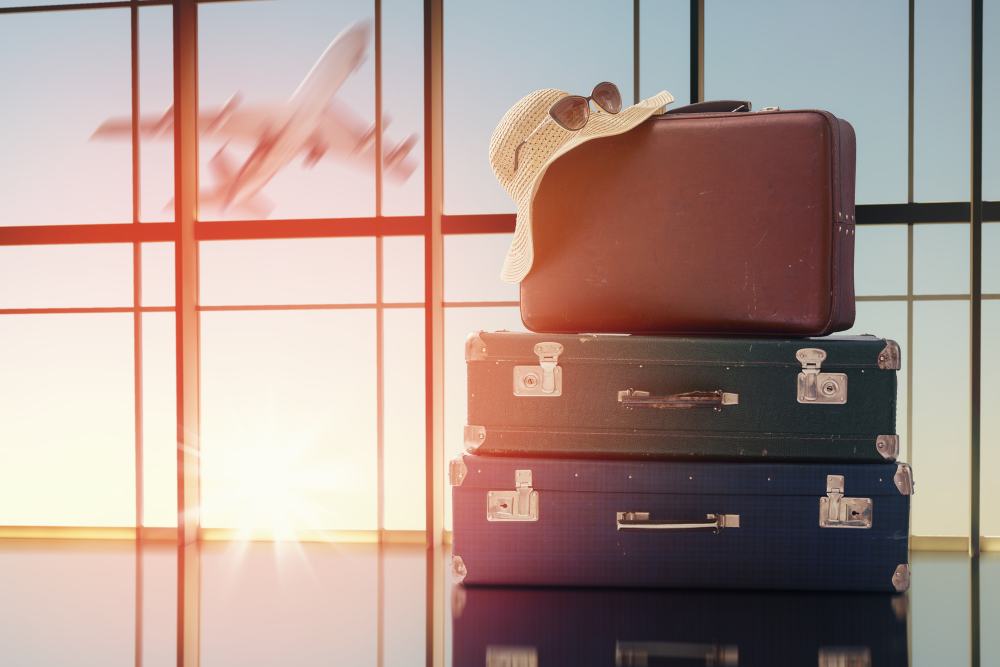 Airport terminal, luggage stack with sunhat and sunglasses, framed by large windows, soft sunrise light, editorial travel photo, no people.