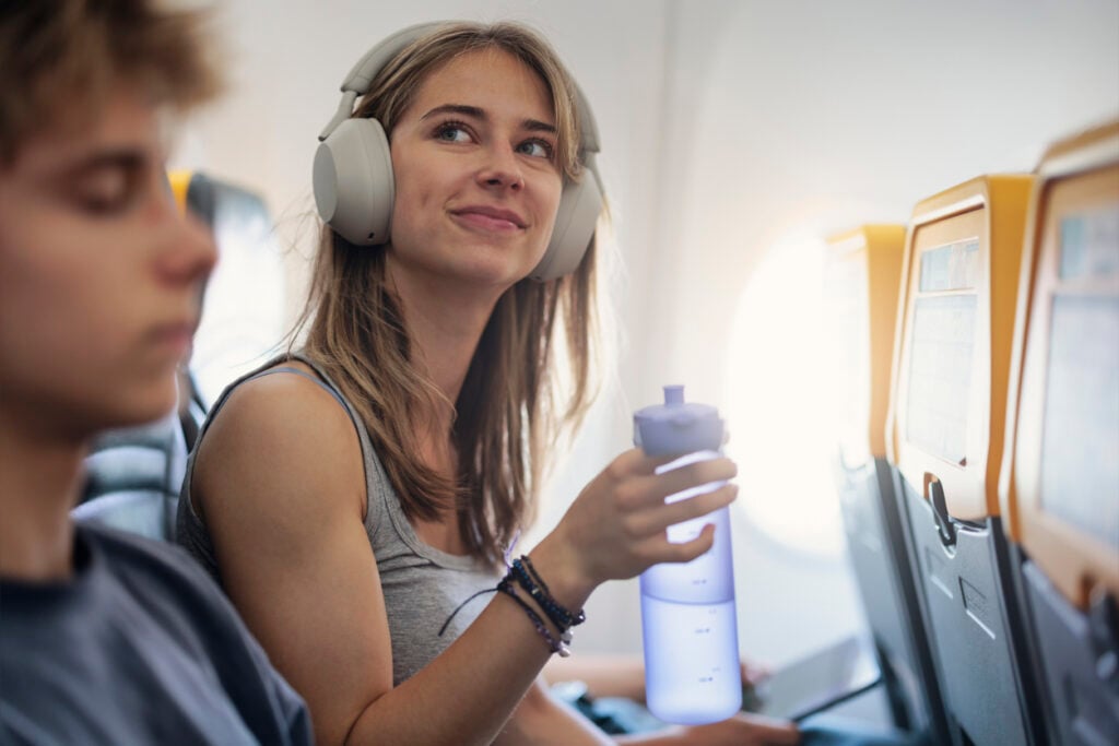 Airplane cabin, woman with headphones smiling, close-up two passengers, daytime lighting, editorial travel photo, people.