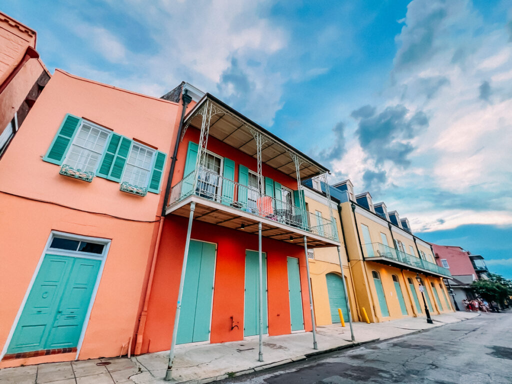 Charming street, pastel facades, turquoise doors, green shutters, cloudy daytime sky, editorial travel photo, no people.