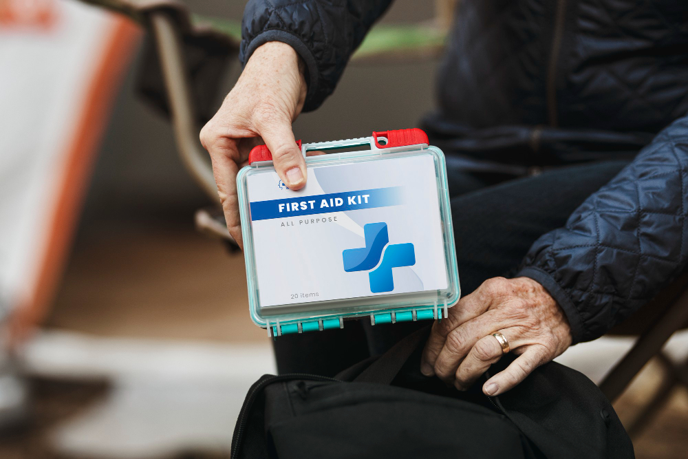 Indoors, clear first aid kit with blue cross, close-up on hands packing black bag, neutral lighting, editorial travel photo, one person.
