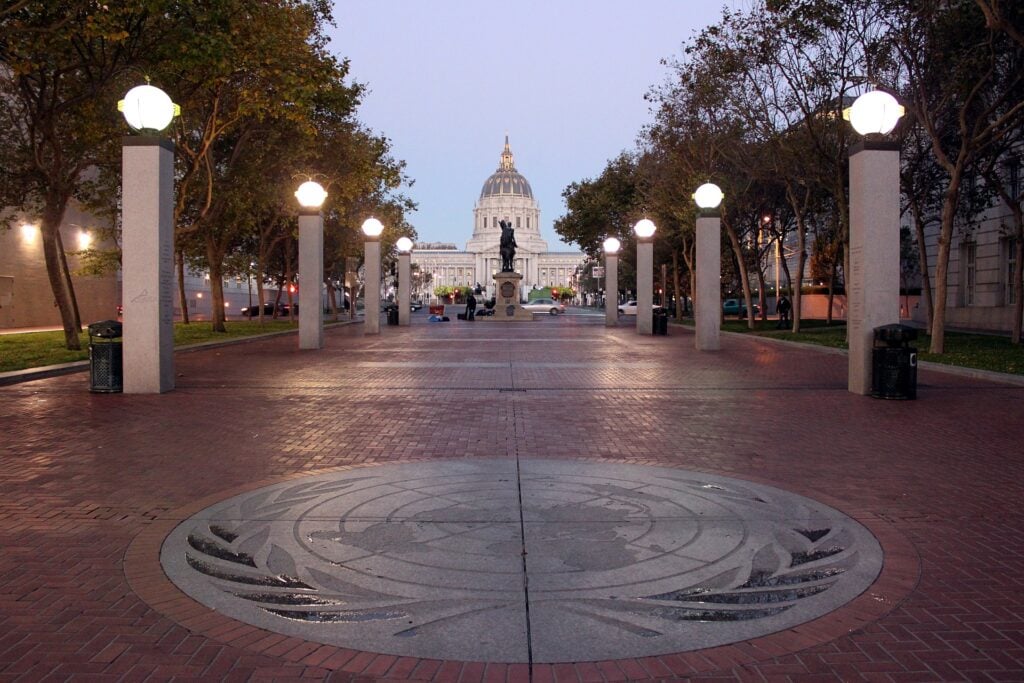 Domed government building, brick walkway, lamp posts aglow, circular design foreground, dusk light, editorial travel photo, no people.