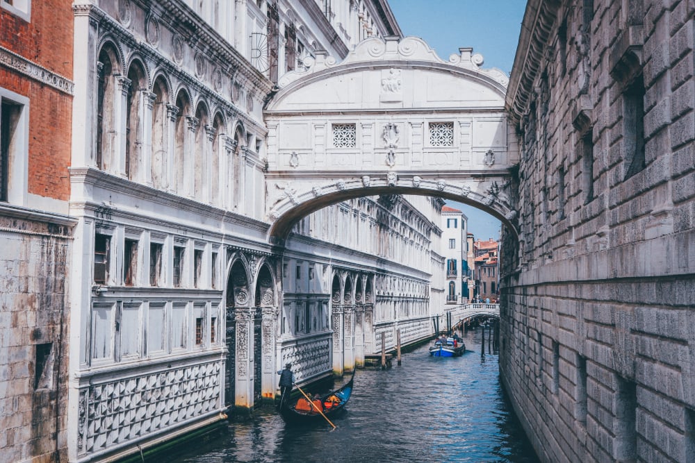 Venice, Bridge of Sighs; white stone arch over narrow canal; gondolas beneath; midday light; editorial travel photo; no people.