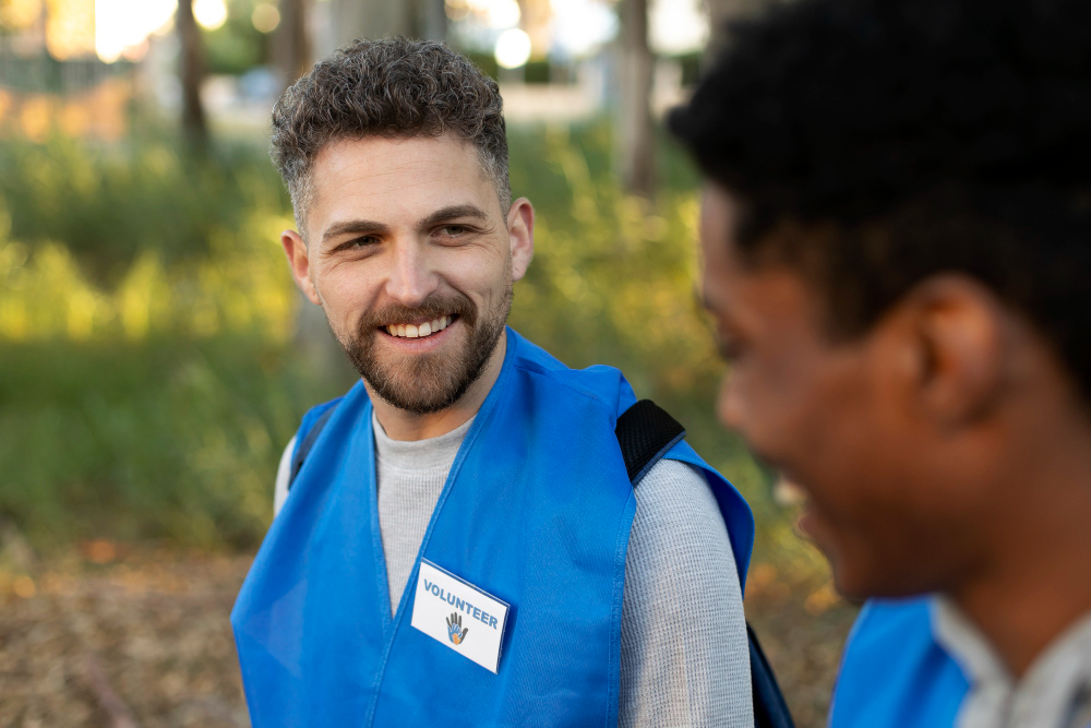 Outdoor park, volunteers in blue vests, candid side view, daylight, documentary style, two people.