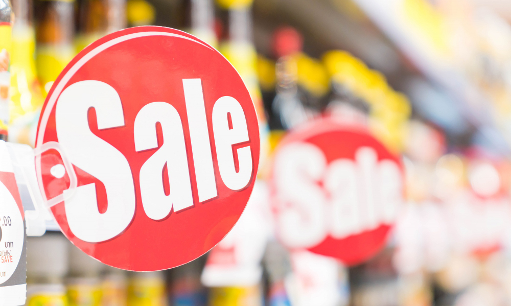 Store aisle, oversized red and white Sale sign, foreground focus, bright overhead lighting, editorial travel photo, no people.