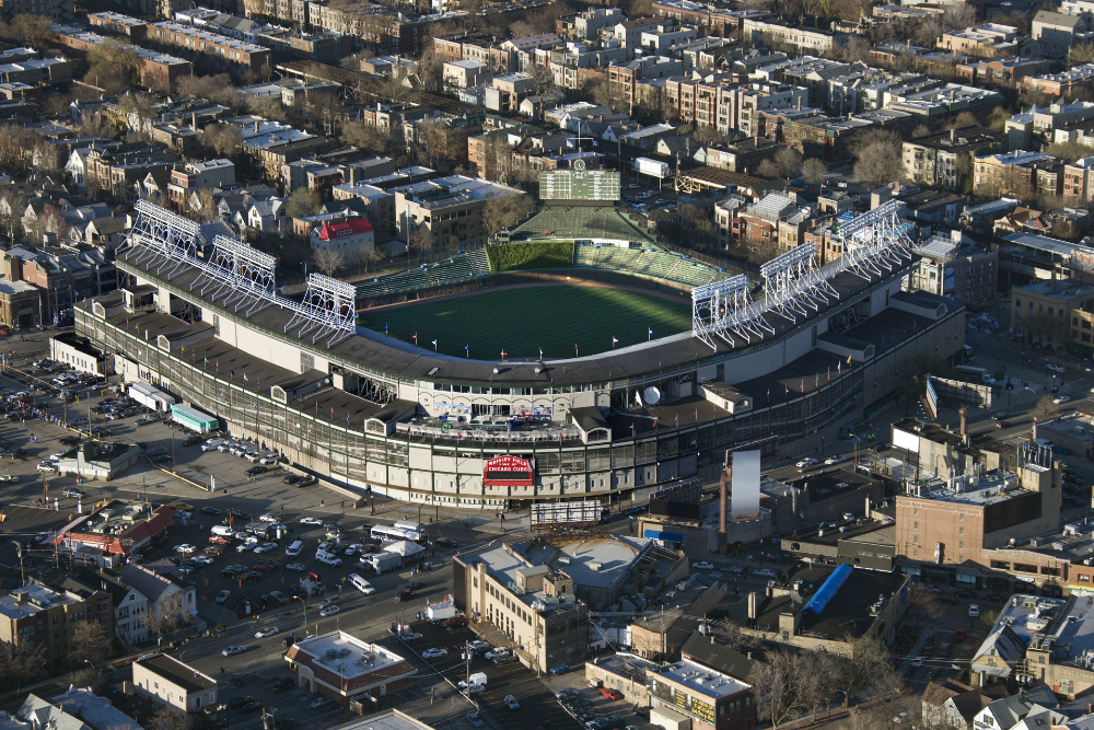 Baseball stadium, empty stands focus, city buildings surround, midday sunlight, editorial travel photo, no people.