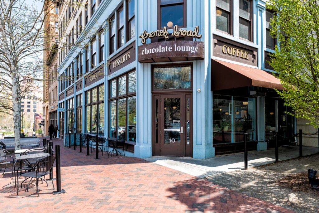 French Broad Chocolate Lounge, blue facade, outdoor seating in foreground, spring sunlight, editorial travel photo, no people.