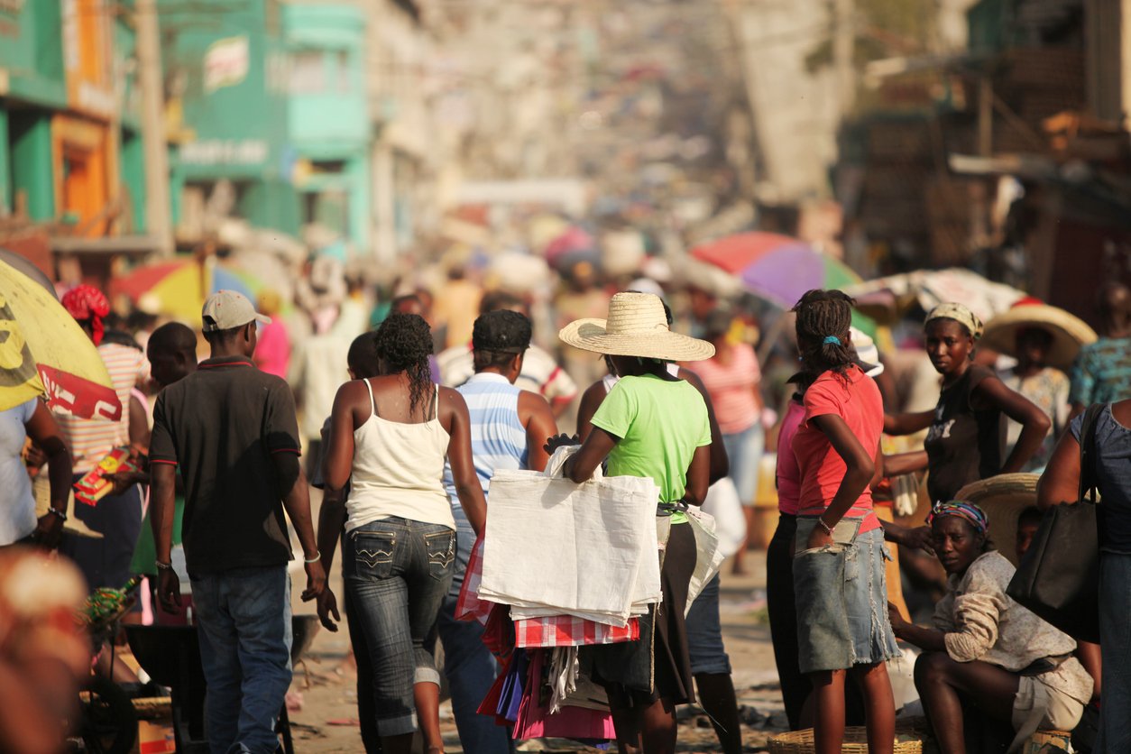 Outdoor market, crowd shopping, vibrant stalls and umbrellas, midday sun, editorial travel photo, many people.