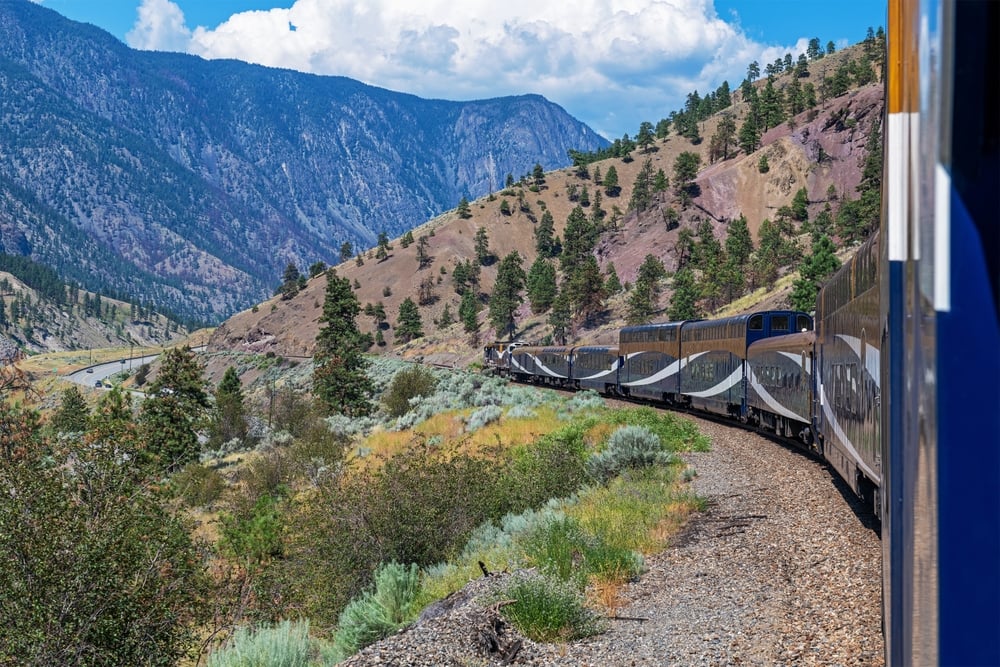 A train travels through a mountainous landscape with trees and clear skies.