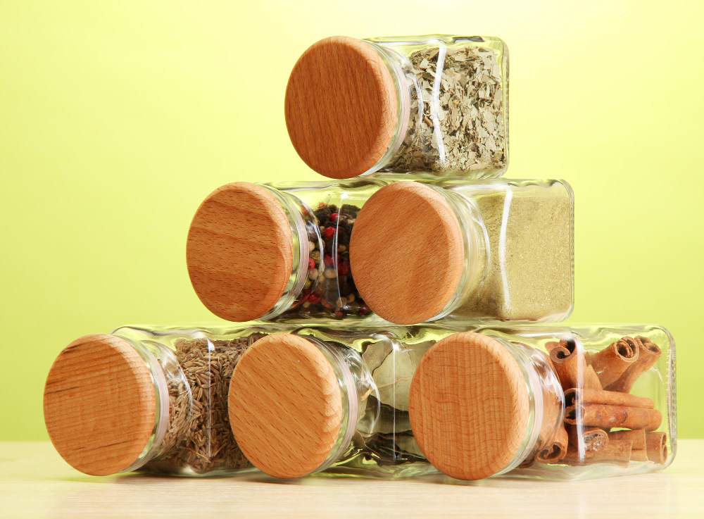 Wooden table, glass spice jars stacked pyramid, soft daylight, light green backdrop, editorial travel photo, no people.