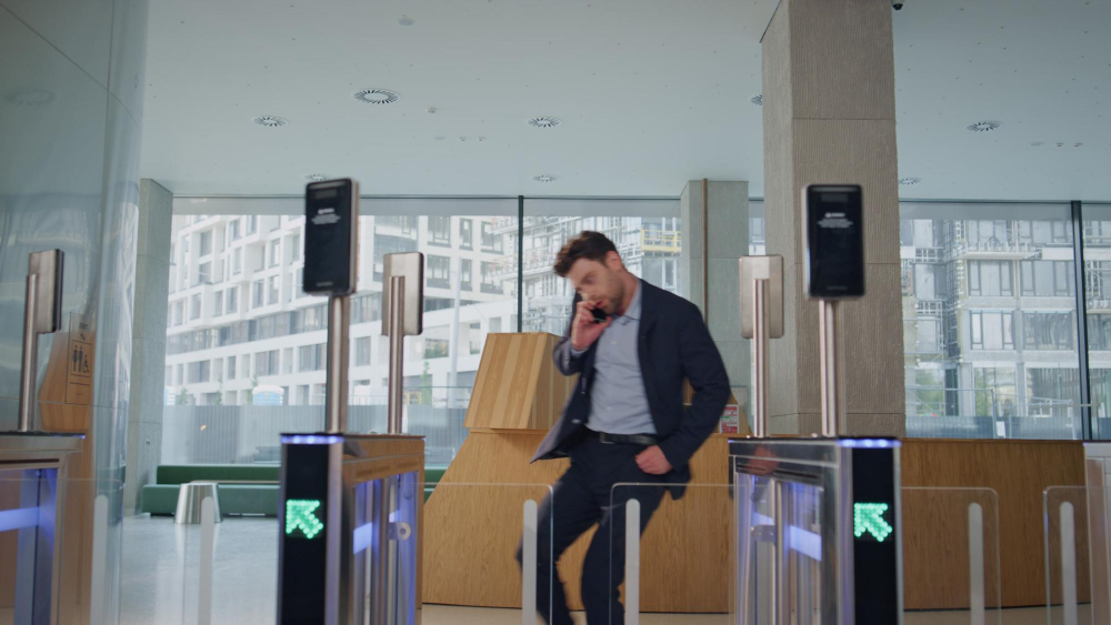 Office lobby, business traveler at security gate, wide windows frame cityscape, midday sunlight, editorial travel photo, one person.