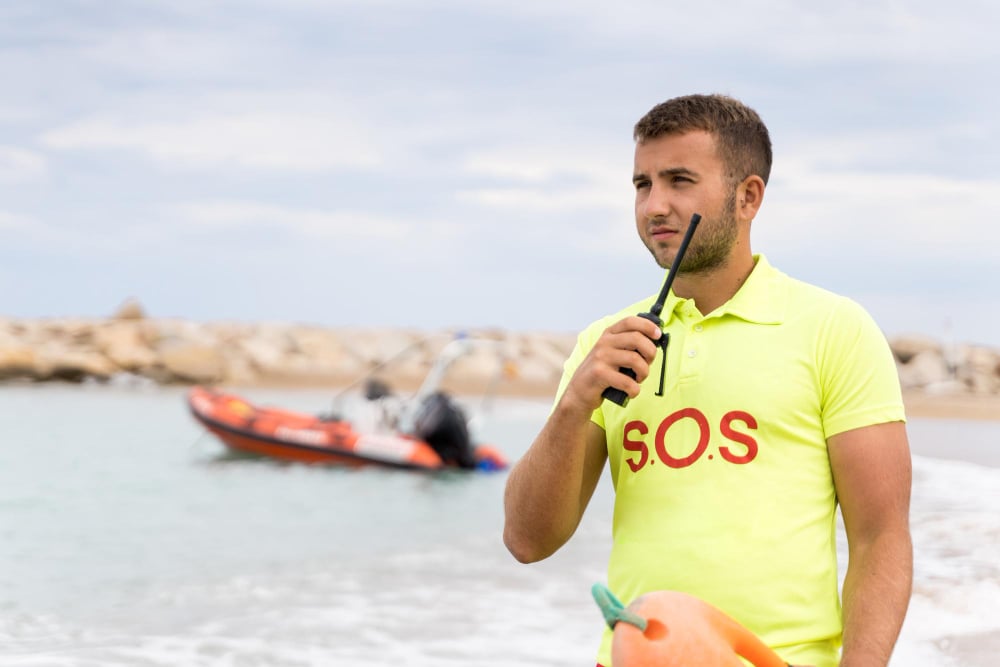 Beach, lifeguard with rescue float, foreground close-up, daytime sunlight, editorial travel photo, single person present.
