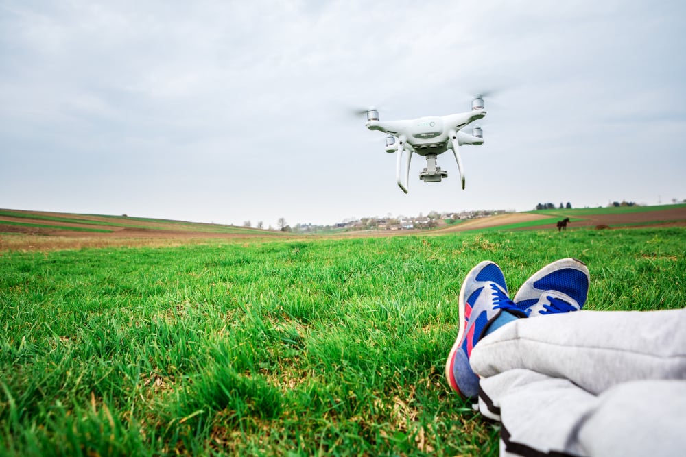 Field with rolling hills, drone hovering above person in gray pants, cloudy sky, wide angle, editorial travel photo, one person.