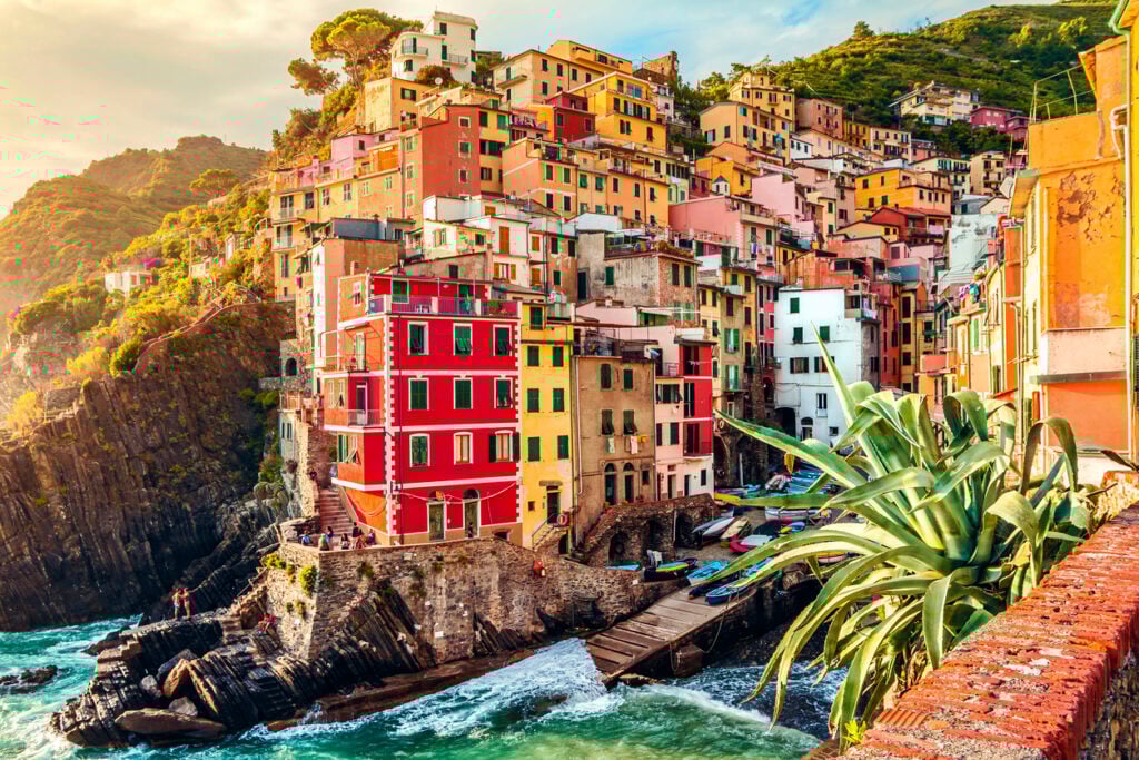 Riomaggiore hillside, vibrant houses, framed by cliffs and greenery, warm sunset glow, editorial travel photo, no people.