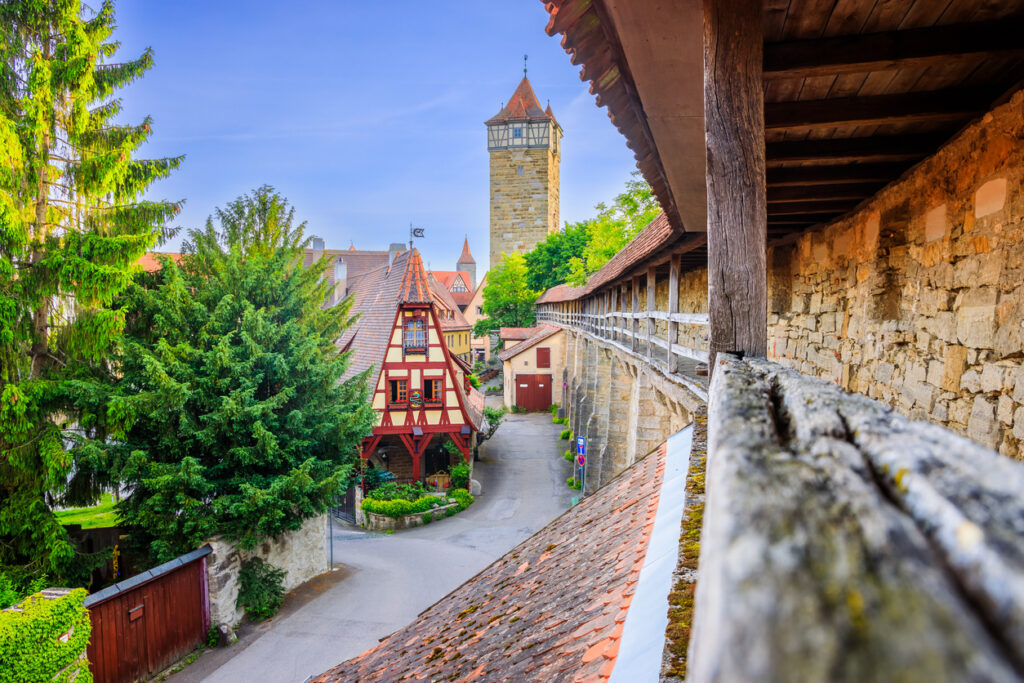 Medieval stone wall and timber-framed house with tower in Rothenburg ob der Tauber, Germany, under a clear sky.