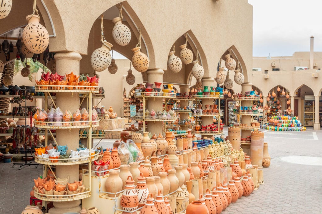 Outdoor market displaying colorful pottery, vases, and decorative hanging lamps under arched stone structures.