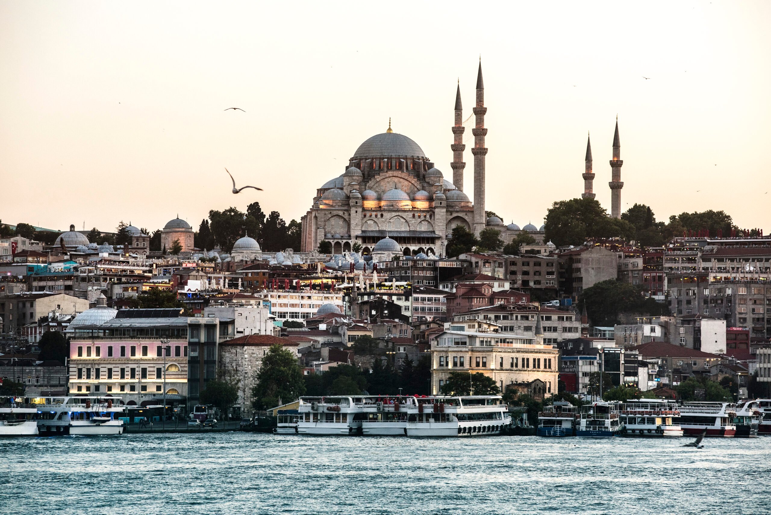 Istanbul, Süleymaniye Mosque gleaming, foreground boats and dense cityscape, sunset glow, editorial travel photo, no people.