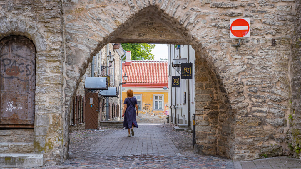 Old cobbled street, red-haired walker, stone archway centered, midday sun, editorial travel photo, single person present.
