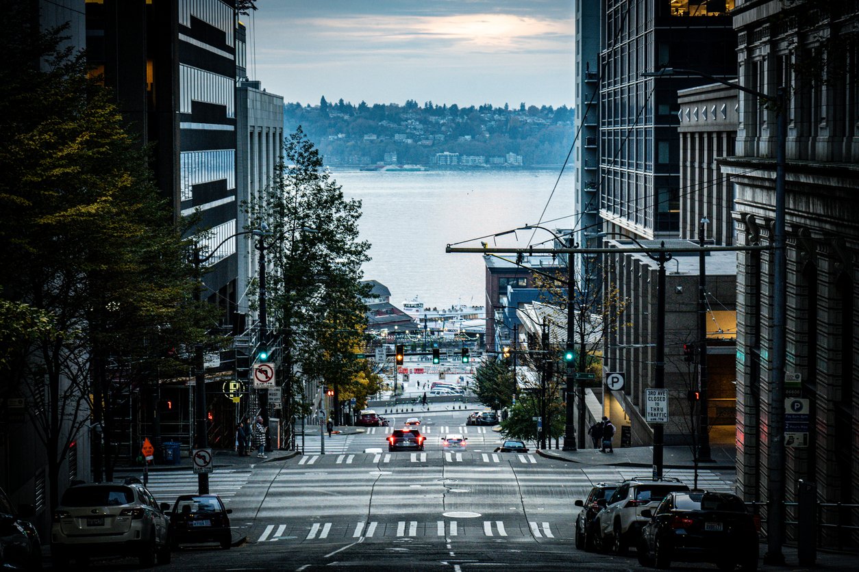 City street, sloping downhill, waterfront view, cloudy daylight, editorial travel photo, no people.