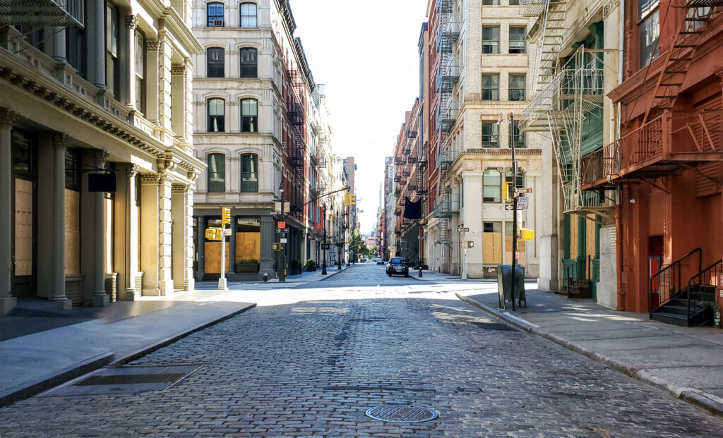 Cobblestone street in SoHo, New York, lined with historic buildings and fire escapes, under clear skies.
