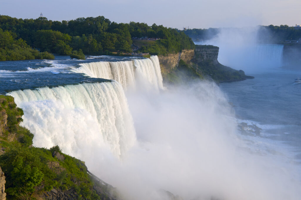 Waterfall cascading over cliffs surrounded by lush greenery, with mist rising above the water below.