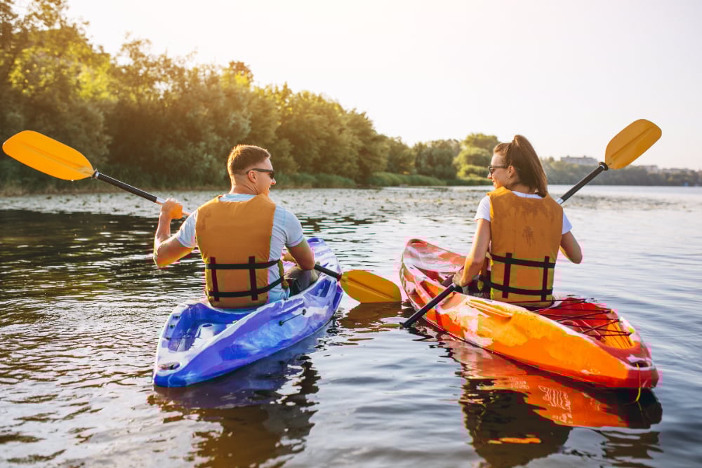 Calm lake, two kayakers in life jackets, mid-frame facing each other, sunny day, editorial travel photo, people present.