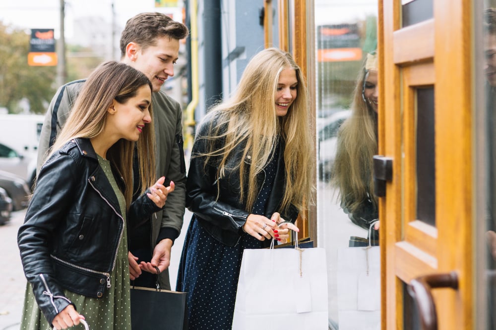 Shopfront, trio with shopping bags, grouped side-by-side, daytime, editorial travel photo, happy young adults.