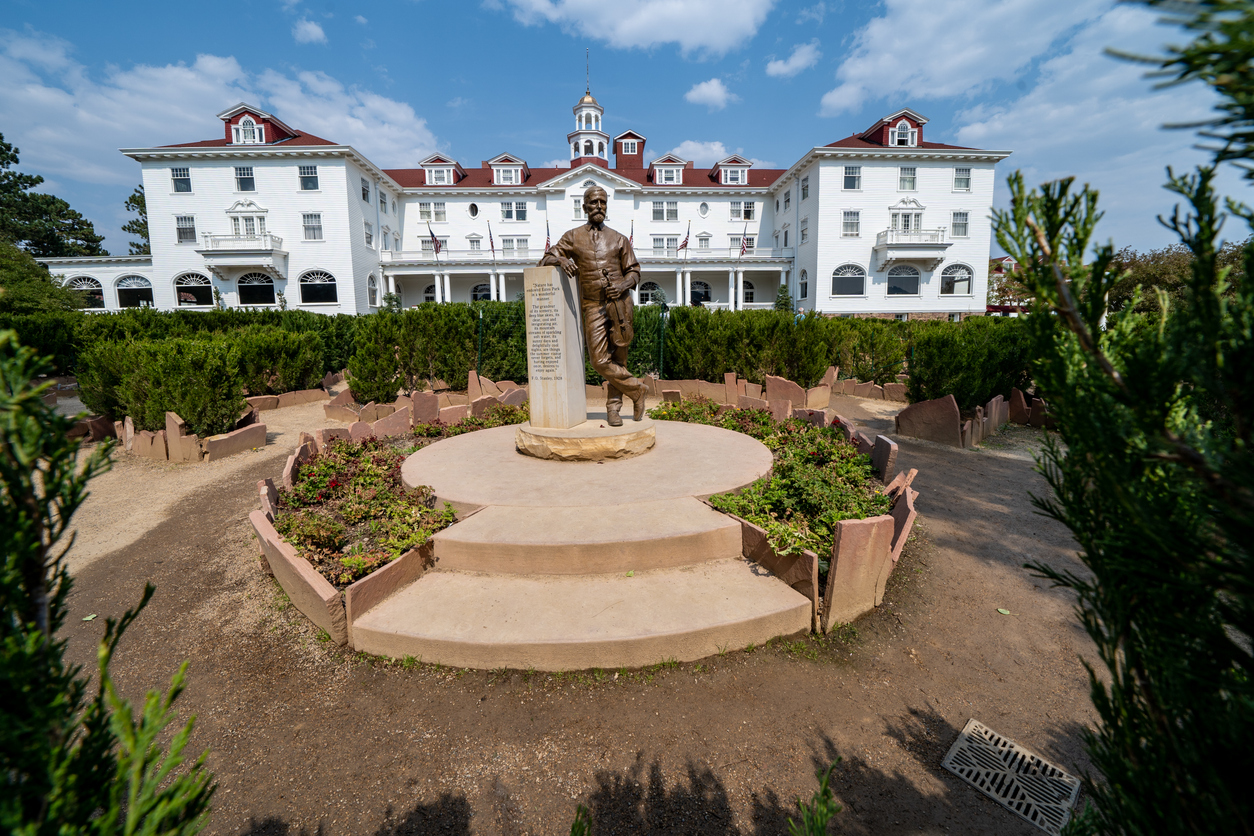 Grand hotel with red roofs, bronze statue foreground, circular pedestal, daytime clouds, editorial travel photo, no people.