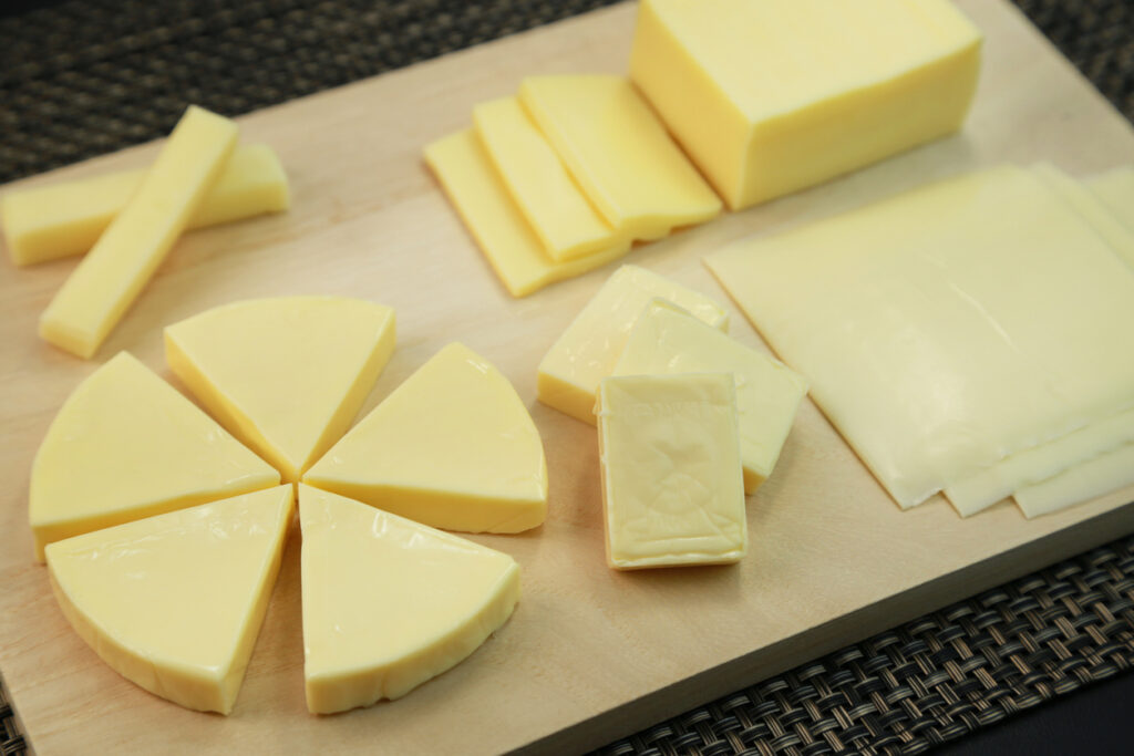 Woven mat surface, wooden cheese board, assorted yellow cheese forms, natural light, editorial travel photo, no people.