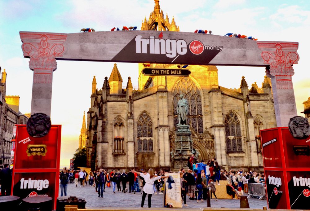 Edinburgh, stone Fringe archway, cathedral backdrop, midday light, editorial travel photo, bustling crowd.