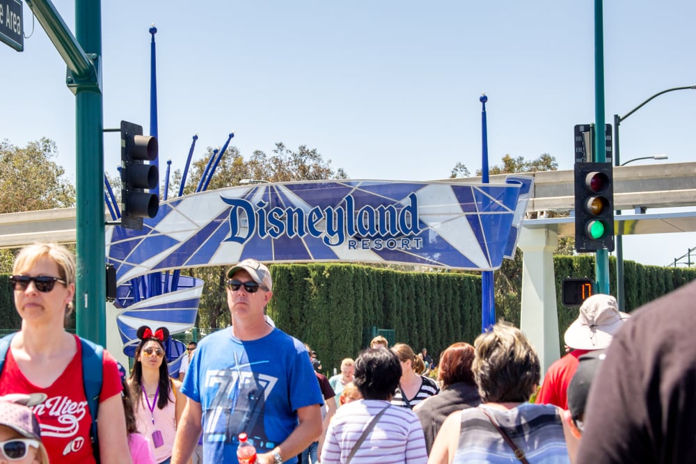 Disneyland Resort entrance, pedestrian crowd, front-facing shot, bright daylight, editorial travel photo, with people.