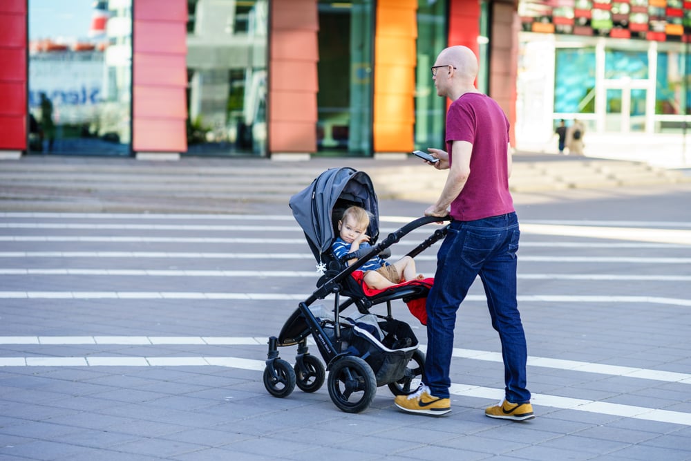 Urban plaza, man and stroller foreground, wide shot, bright daylight, editorial travel photo, people.