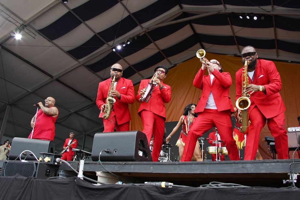 Band in red suits performing on stage with saxophones, trumpet, and other instruments.