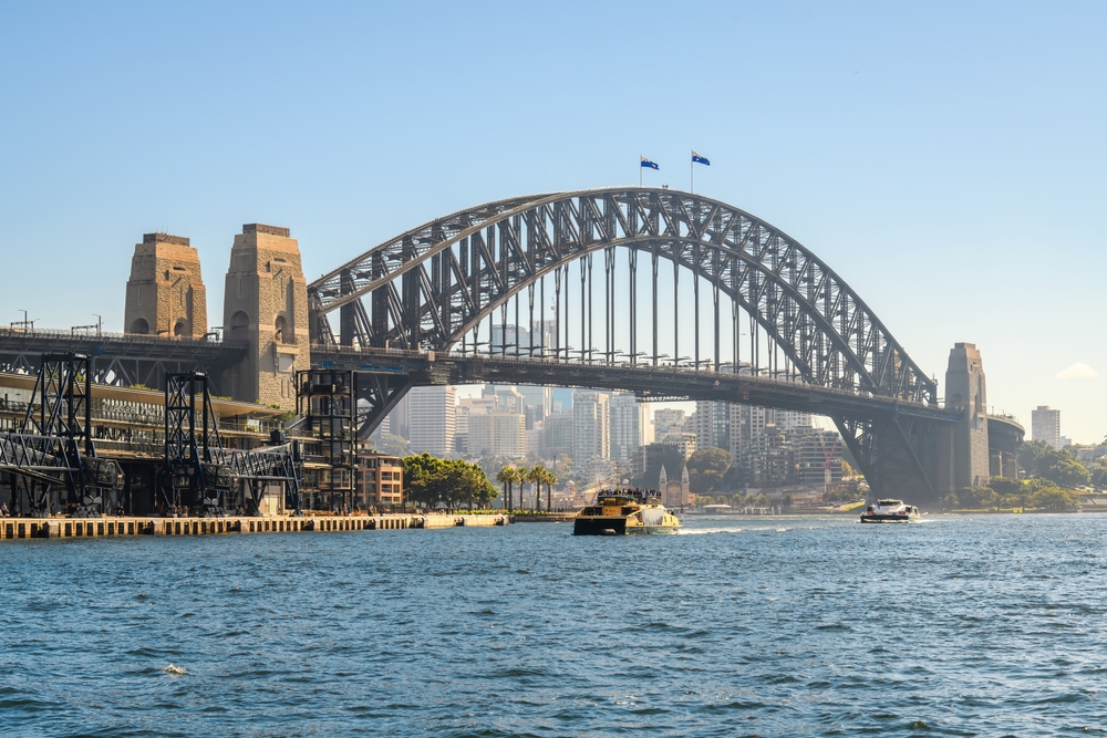 Sydney Harbour Bridge over water with boats and city skyline in background.