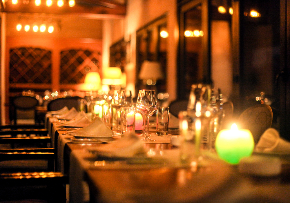 Restaurant interior, long dinner table centerpiece, symmetrically arranged glassware and candles, low warm lighting, editorial travel photo, no people.