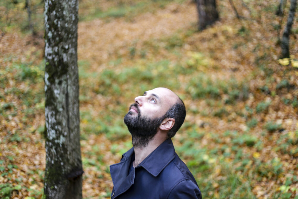 Bald man with a beard looking up in an autumn forest with fallen leaves.