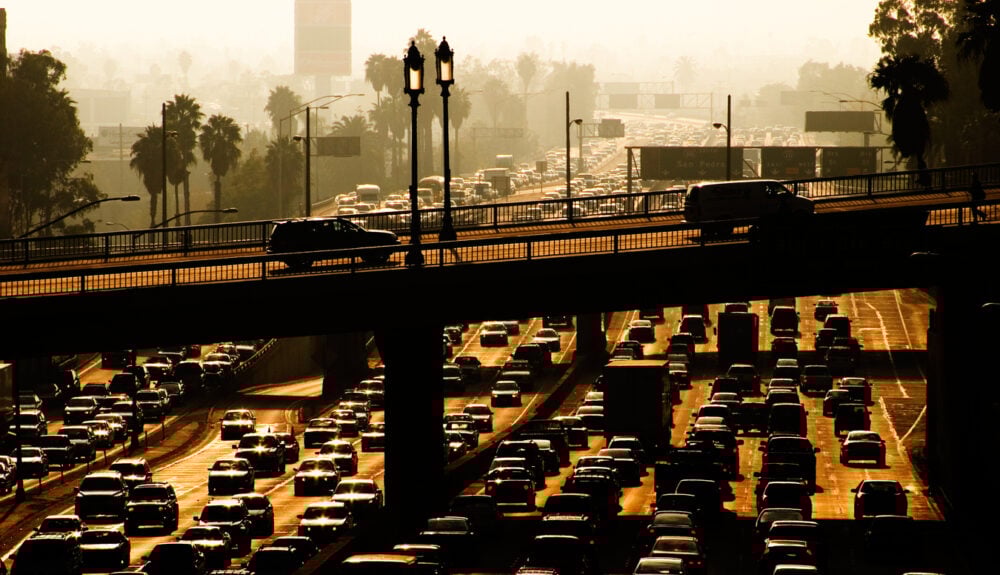 City highway, dense traffic jam, layered roadway view, sunset haze, documentary style image, no people visible.