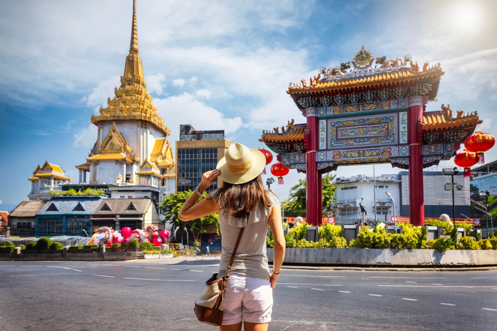 Golden temple and red Chinese gate with lanterns, woman admiring view, wide shot, sunny day, editorial travel photo, one person.
