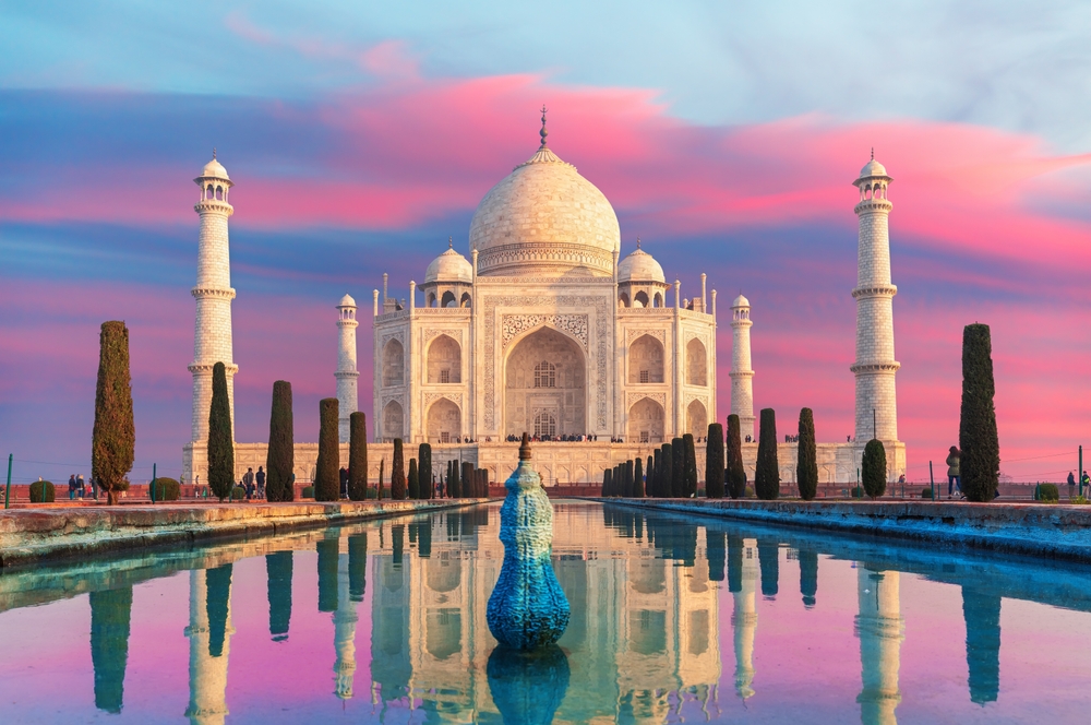 The Taj Mahal with reflecting pool at sunset, vibrant pink and blue sky.