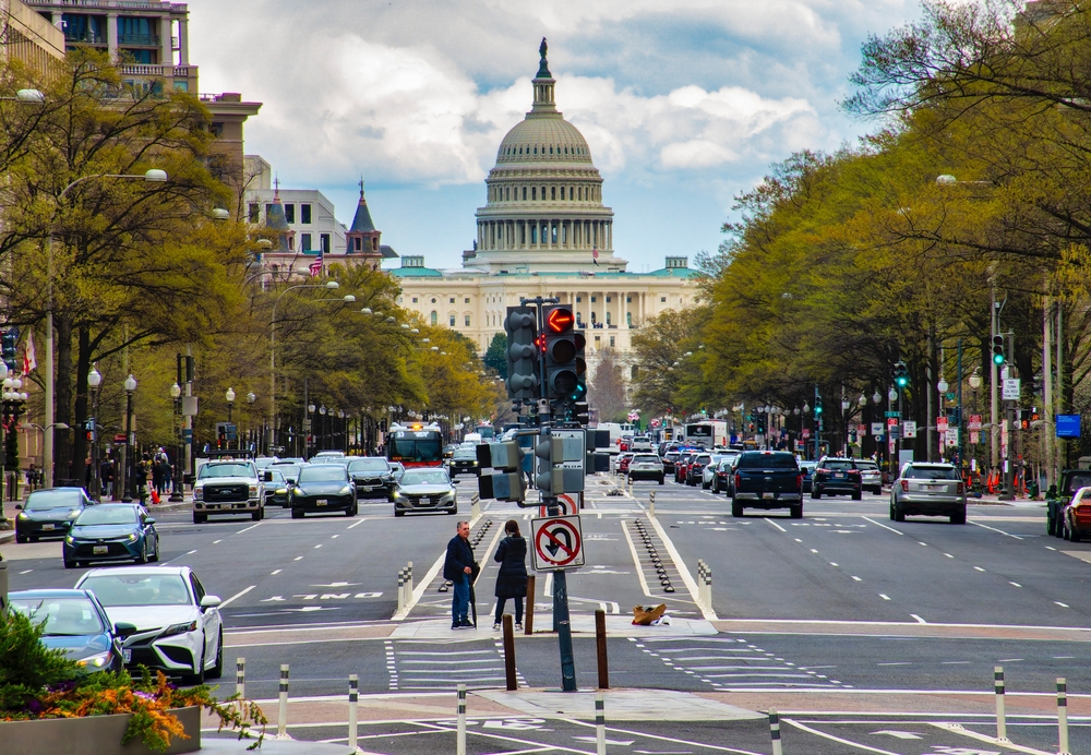 Street view of U.S. Capitol with cars, trees, and traffic lights in foreground.
