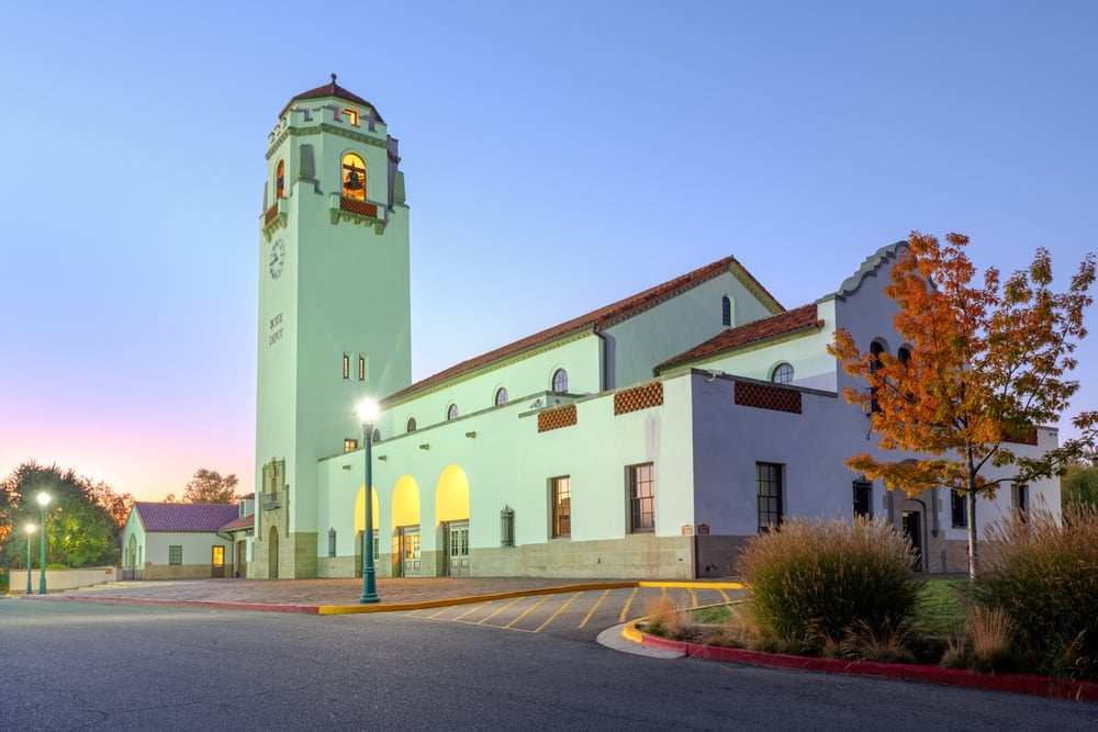 White building with clock tower, arched windows, autumn tree, and lamp post under a clear blue sky at dusk.