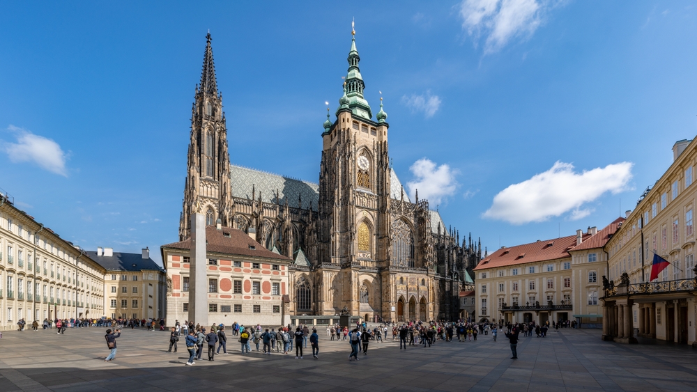 Gothic cathedral with two tall spires and ornate facade in a busy courtyard under a blue sky.