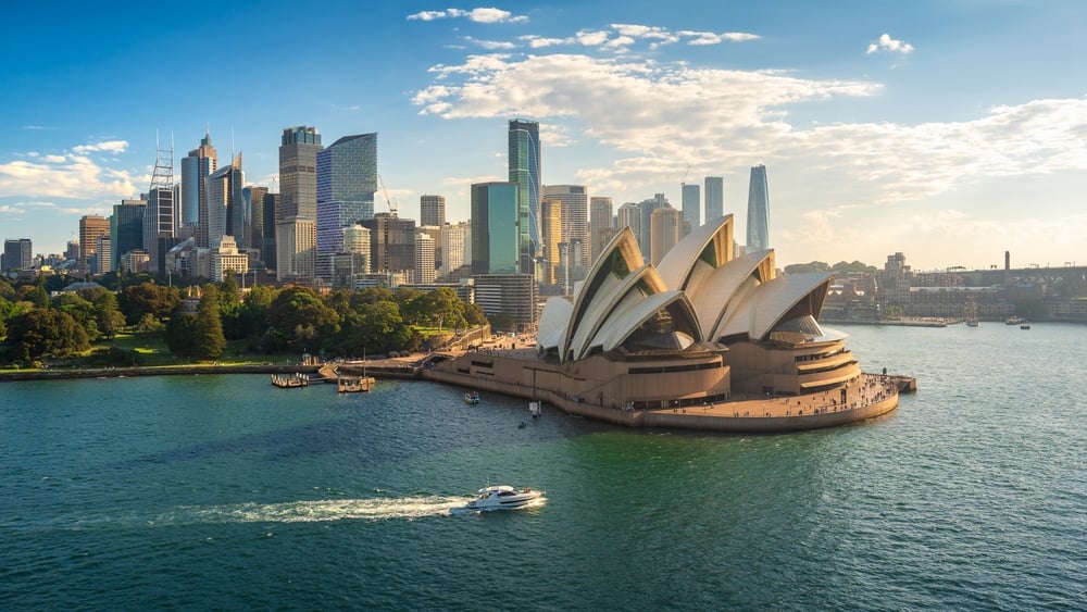 Sydney Opera House with a boat on the harbor, modern city skyline in the background.