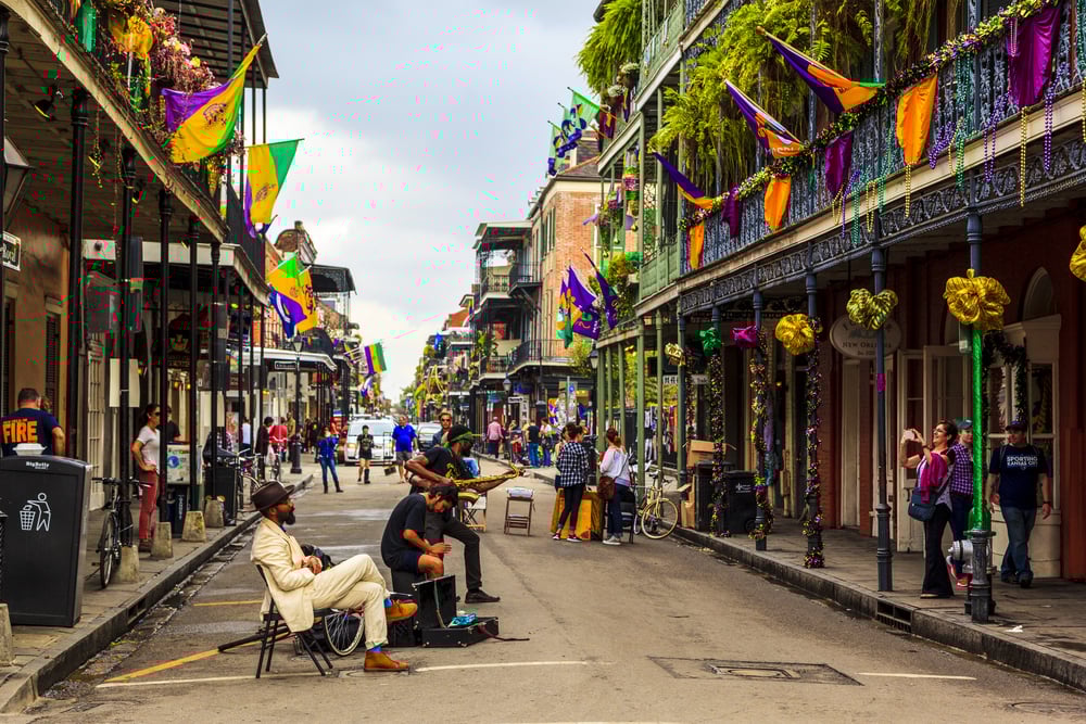 Street musicians performing in a festive, decorated street with colorful flags and bystanders in New Orleans.