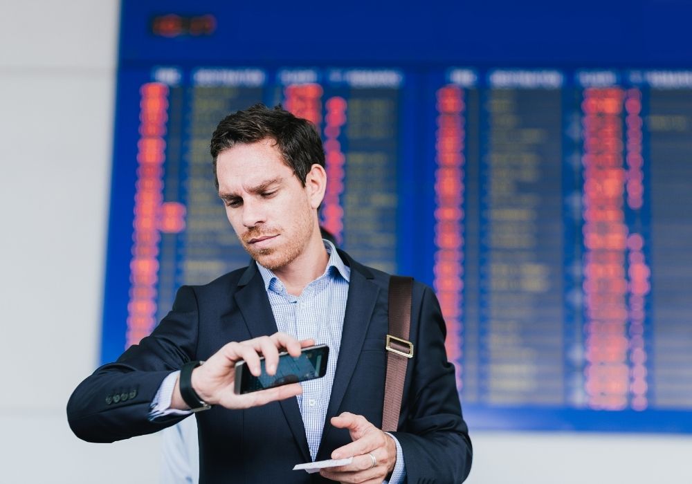 Airport terminal, man in suit, glancing at watch, phone in hand, midday lighting, editorial travel photo, single traveler.