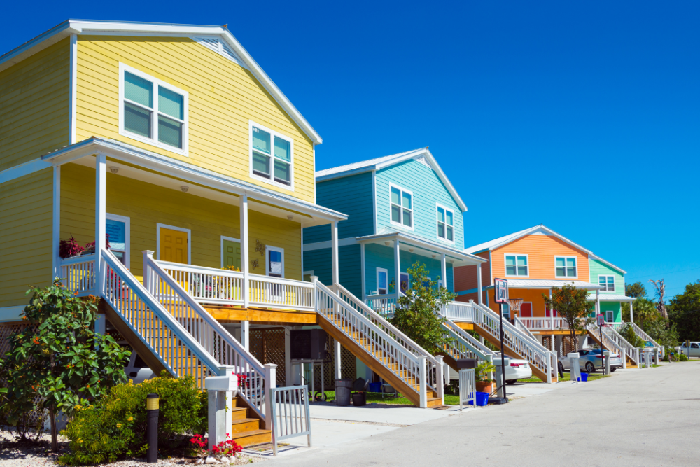 Three colorful houses with stairs, each painted yellow, blue, and orange, under a clear blue sky.