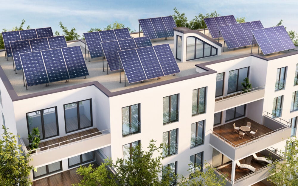 White building with rooftop solar panels, multiple balconies, and surrounded by trees.