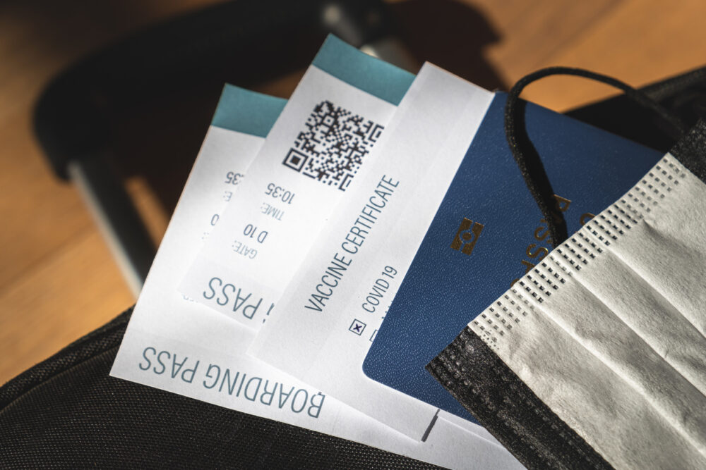 Boarding passes, vaccine certificate, passport, and face mask on a suitcase.