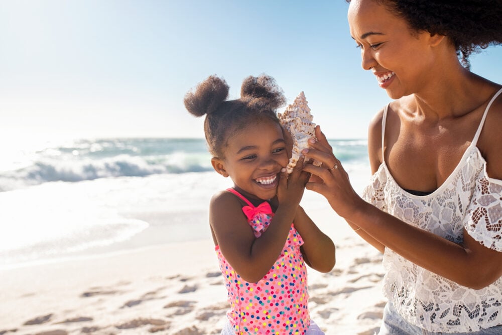 Woman and child enjoying a conch shell at the beach on a sunny day.