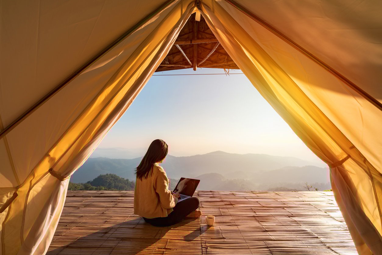A person sitting with a laptop in a tent with a mountain view at sunrise.
