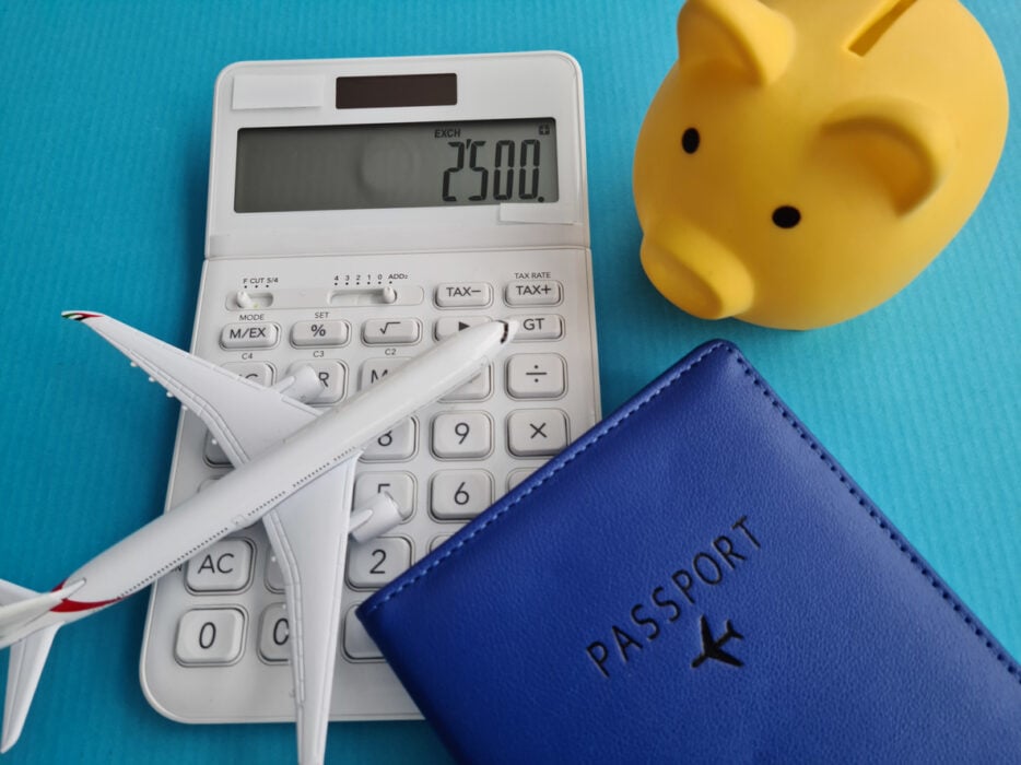 White calculator, toy airplane, blue passport, and yellow piggy bank on a blue surface.